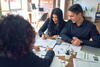 a woman signs documents with a man at a table all the while guided by a third person helping them